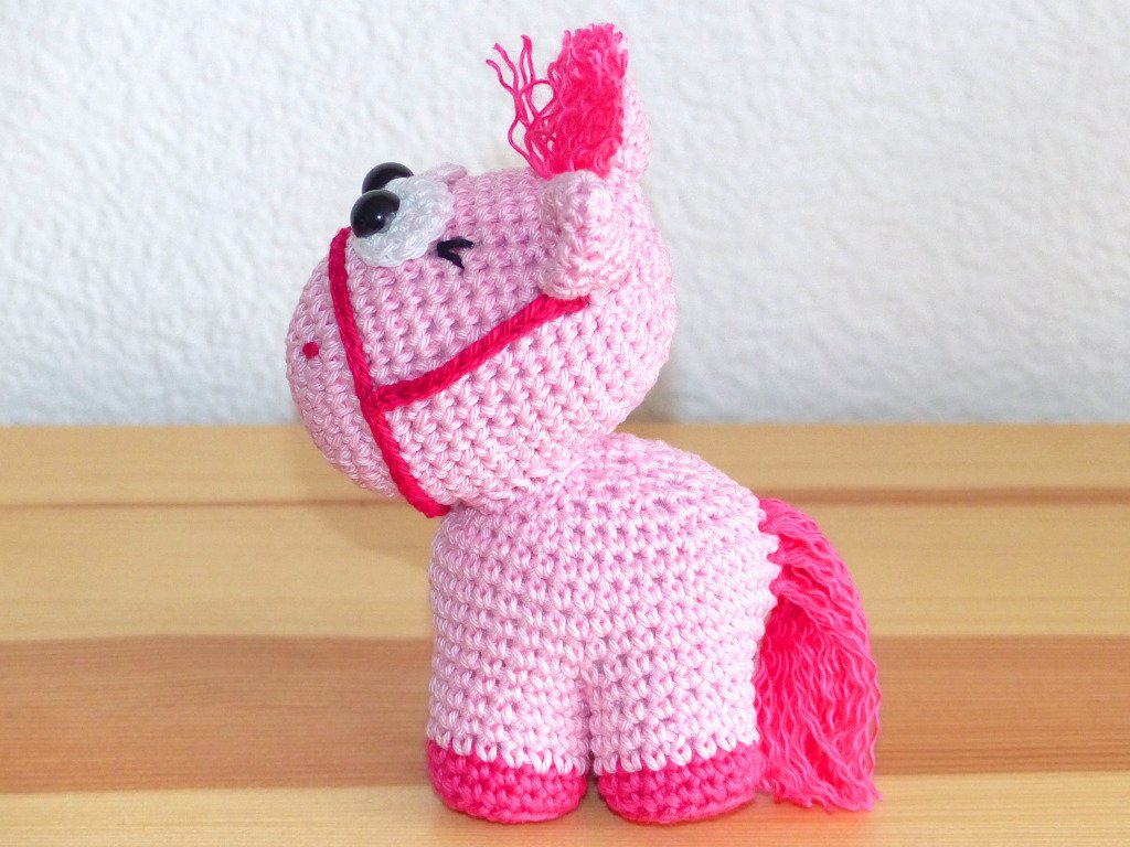 Gehäkeltes rosa Amigurumi-Pferd mit pinker Mähne und dunklen Augen, Seitenansicht
