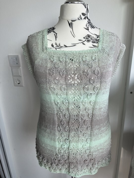 Mint‑beiges Stricktop mit Ajour- und Zopfmuster auf Schneiderpuppe, quadratischer Ausschnitt