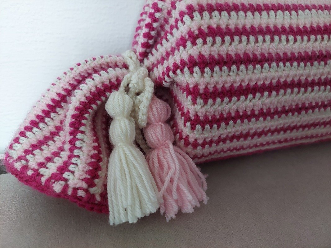 Detailaufnahme gehäkelter rosa- und cremefarbener Streifen und geknoteter Quasten an einem Kissenbezug