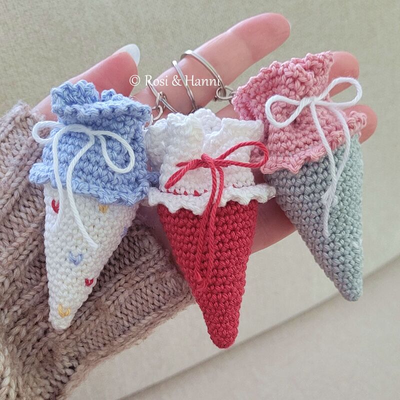 Drei gehäkelte Mini‑Schultüten als Schlüsselanhänger in Pastellfarben an einem Schlüsselring, in einer Hand gehalten.