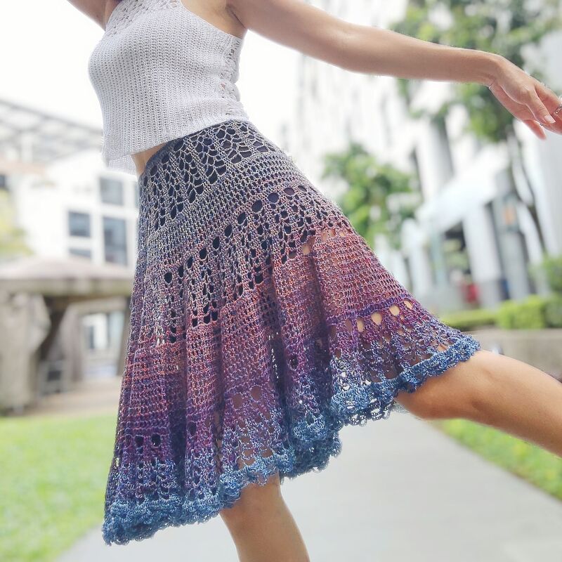 Flared ombré crochet skirt in purple, reddish-purple, and blue with lace motifs and scalloped hem, worn with a white crop top