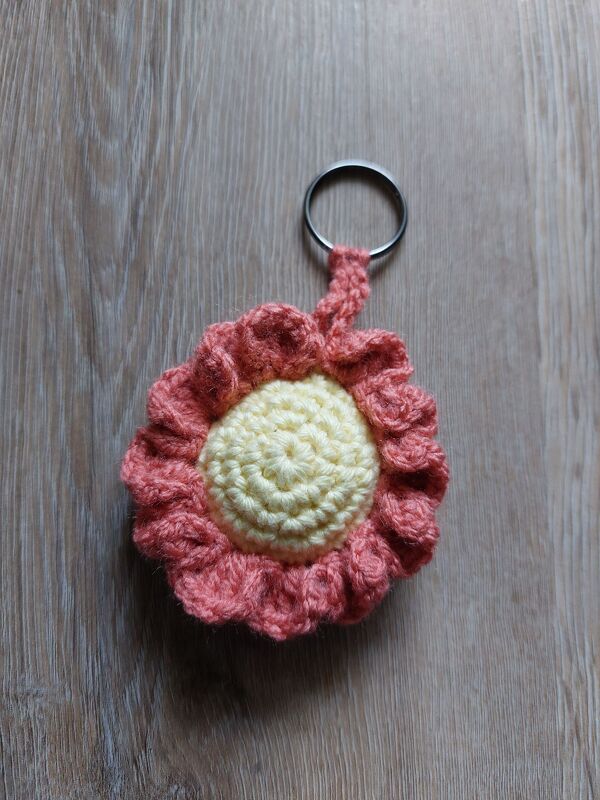 Gehäkelter Blumen-Schlüsselanhänger in Koralle und Gelb auf Holz