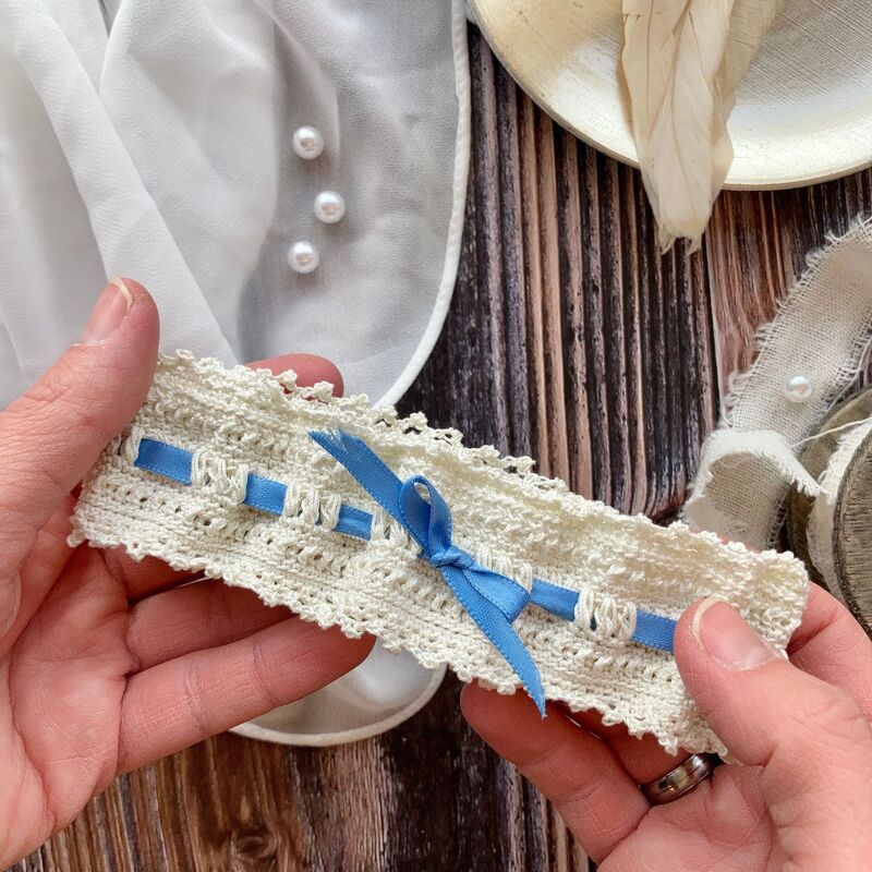 Hands holding an ivory crocheted lace wedding garter threaded with a blue ribbon and bow