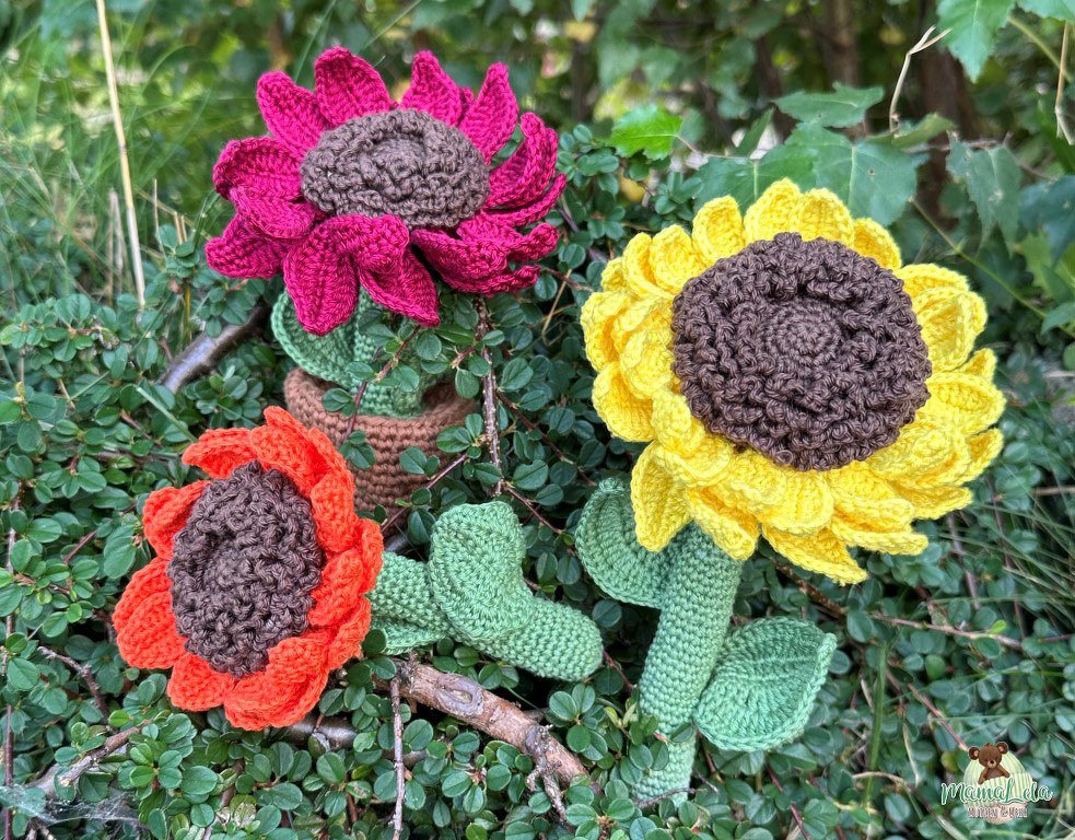 Farbenfrohe gehäkelte Blumen in Gelb, Pink und Orange mit braunen Kernen und grünen Blättern