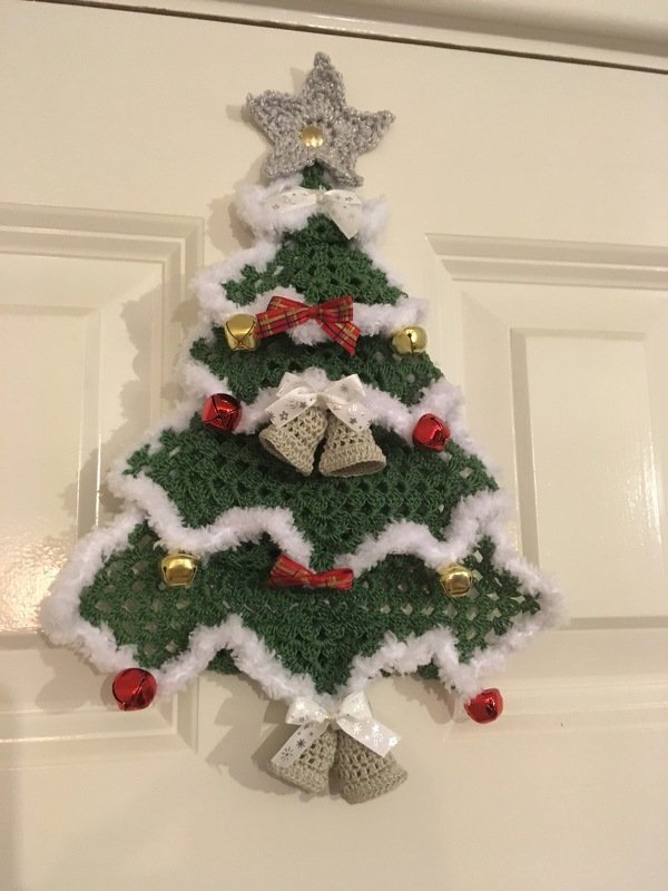 Crocheted green Christmas tree door hanger with white trim, bells, bows and silver star