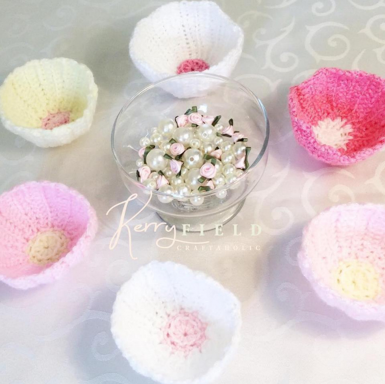Petal-shaped crochet bowls in pastel pink, white and yellow arranged around a bowl of pearls and ribbon roses