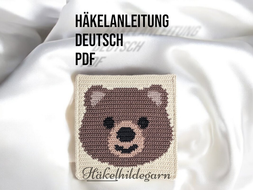 Gehäkeltes Pixelquadrat mit braunem Bärenkopf auf hellbeigem Untergrund