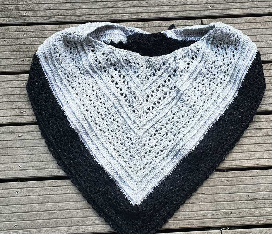 Gehäkeltes Dreieckstuch in Hellgrau mit schwarzer Randborte auf Holzuntergrund.