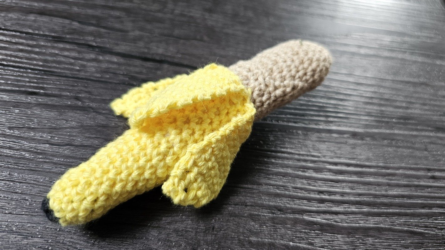Gehäkelte Banane mit gelber Schale und beigem Inneren auf dunklem Holztisch