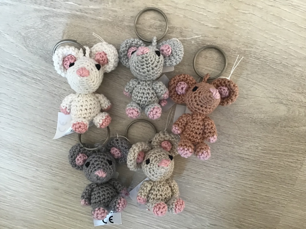 Fünf gehäkelte Amigurumi-Mäuse als Schlüsselanhänger in Pastellfarben auf hellem Holz