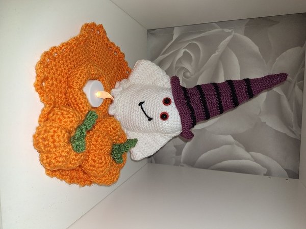 Gehäkelte Halloween-Tischdeko mit weißem Geist, violett-schwarz gestreiftem Hexenhut, orangefarbener Kürbis-Häkelunterlage mit grünen Details und kleinem elektrischem Teelicht.