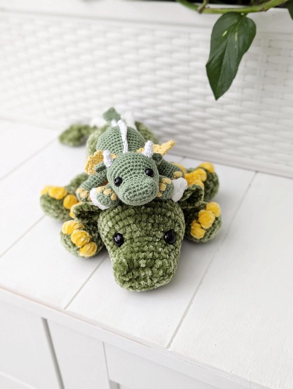 Zwei gehäkelte grüne Drachen-Amigurumi, ein kleiner auf einem größeren liegend