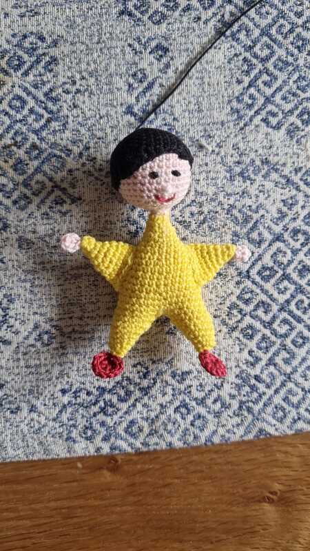 Gehäkelte gelbe Sternfigur mit Kopf und Gliedmaßen auf blau gemustertem Stoff
