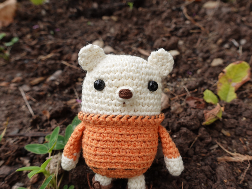Nahaufnahme eines gehäkelten Amigurumi-Teddys mit orangefarbenem Pullover