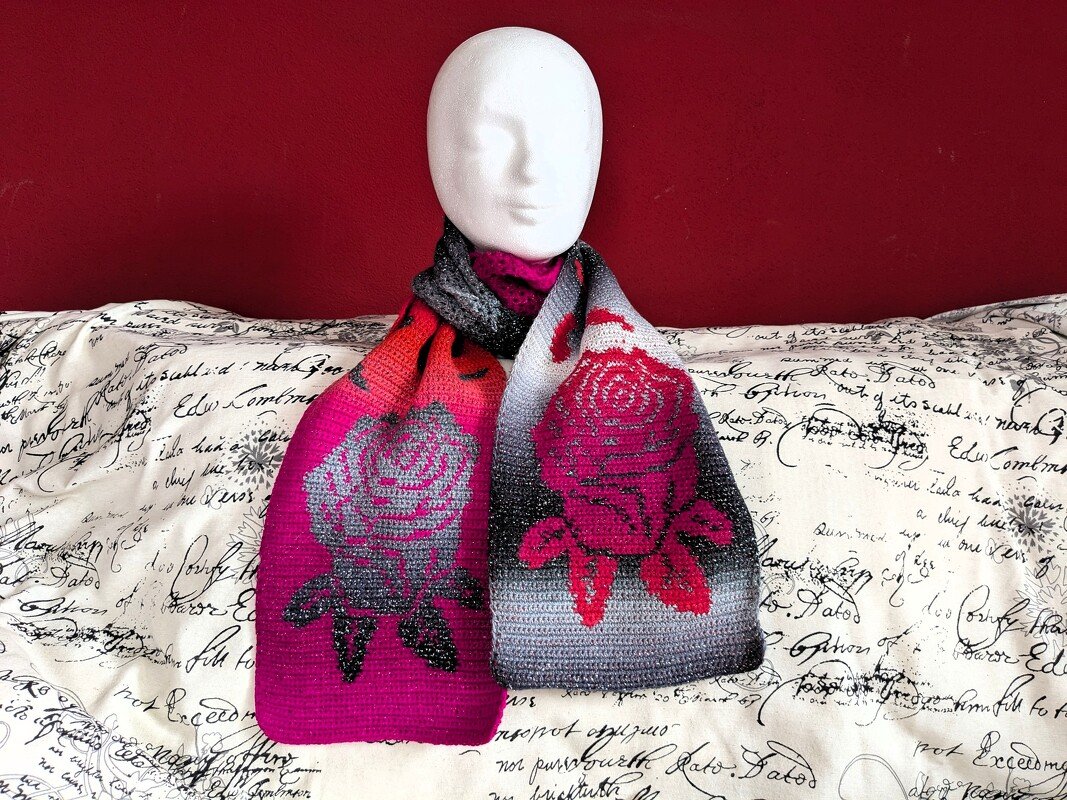 Gehäkelter Schal in Pink, Grau und Schwarz mit Rosenmuster auf einer Schaufensterpuppe vor roter Wand