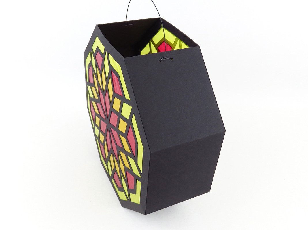 Schwarze sechseckige Papierlaterne mit gelb-rotem Mosaikmuster und Drahtbügel