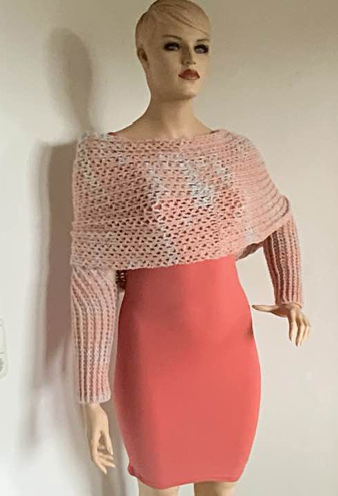 Gehäkelter zartrosa Bolero mit langen Ärmeln und Lochmuster über korallfarbenem Kleid auf Schaufensterpuppe.