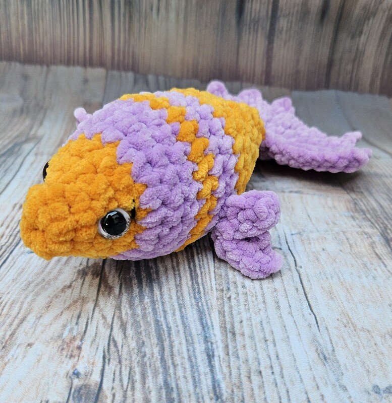 Gehäkelter Amigurumi-Fisch in Orange und Lila auf Holzboden