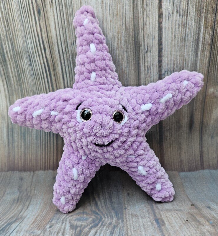 Fliederfarbener Amigurumi-Seestern mit strukturierter Oberfläche, glänzenden Augen und lächelndem Gesicht