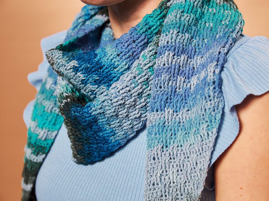 Nahaufnahme eines gehäkelten Tuchs in Blau- und Türkistönen, um den Hals gelegt.