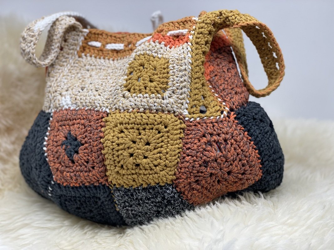 Granny-Square Shopper aus gehäkelten Quadraten in Senfgelb, Rost, Creme und Dunkelgrau auf flauschigem Untergrund