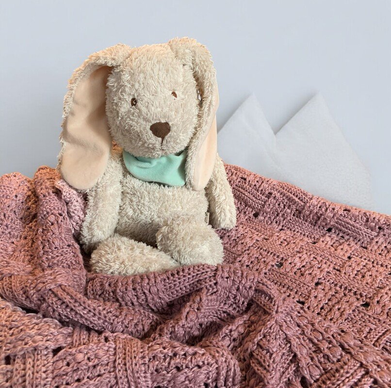 Plüschhase sitzt auf rosé gehäkelter Decke mit strukturiertem Muster