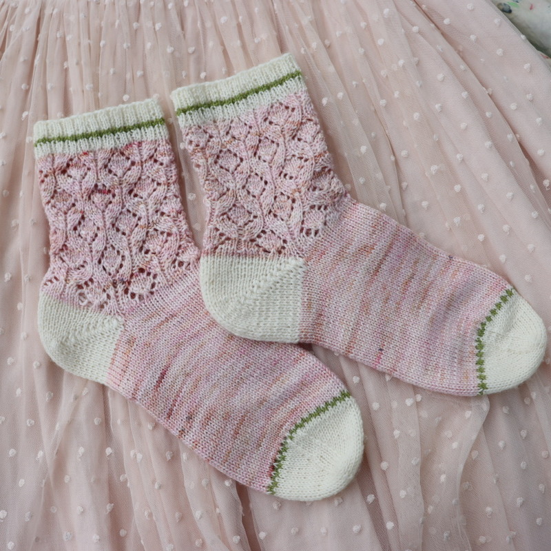 Paar gestrickter pastellrosa Socken mit Ajourmuster, weißen Fersen und grüner Kante