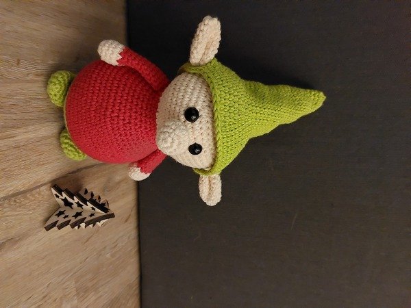 Gehäkelter Amigurumi-Wichtel in Rot und Grün neben kleiner Holz-Weihnachtsdeko