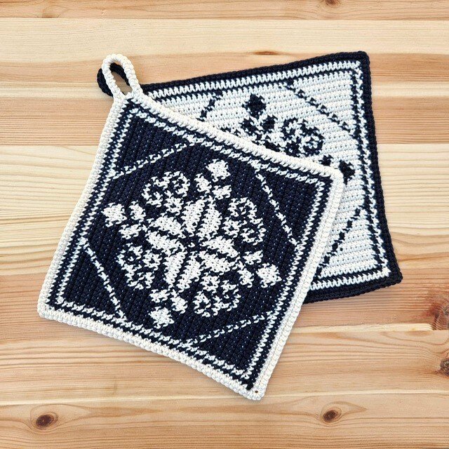 Zwei schwarz-weiße gehäkelte Topflappen mit Schneeflockenmuster auf Holzuntergrund