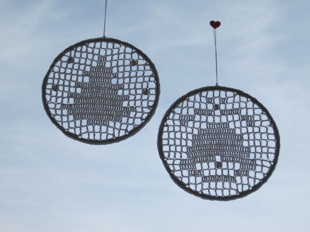 Zwei runde, gehäkelte Anhänger mit Weihnachtsbaum-Motiv vor hellem Himmel