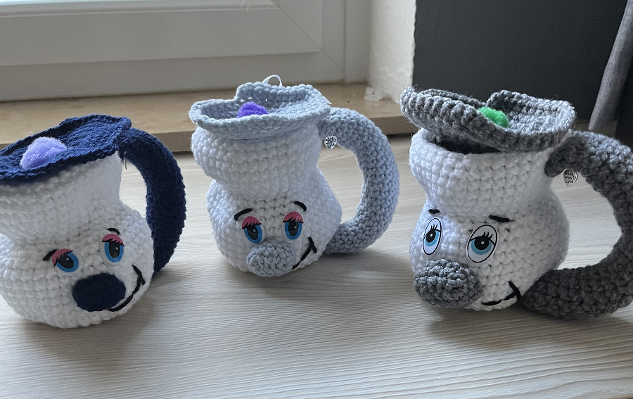 Drei gehäkelte Amigurumi-Tassen mit Griffen und freundlichen Gesichtern