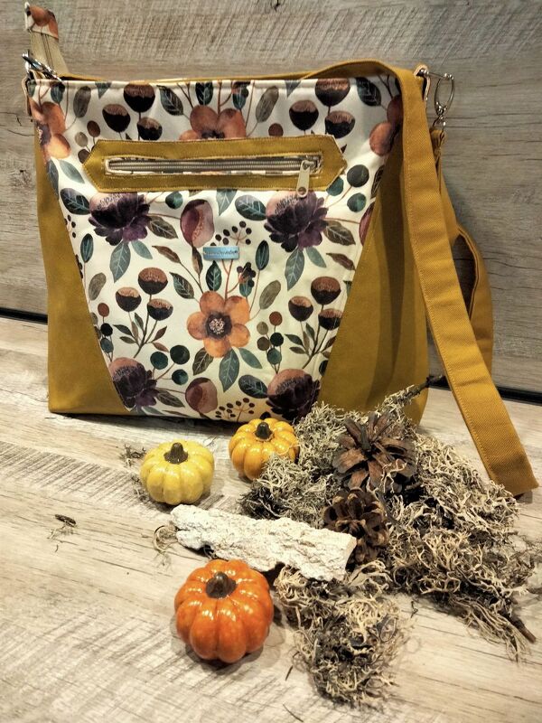 Senfgelbe Schultertasche mit floralem Frontpanel und Reißverschluss auf Holztisch mit Herbstdeko