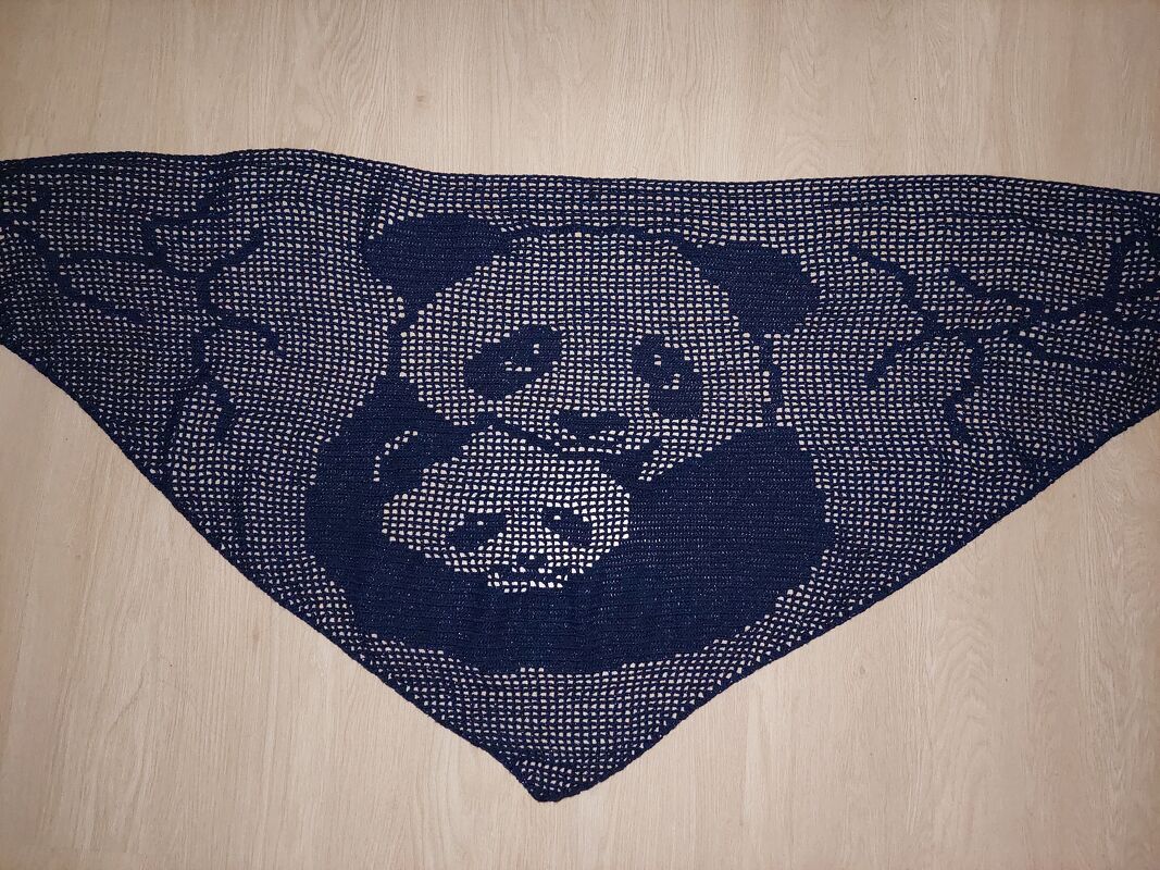 Dunkelblaues gehäkeltes Dreieckstuch mit einem großen Panda, der einen kleinen Panda umarmt, auf hellem Holzboden liegend.