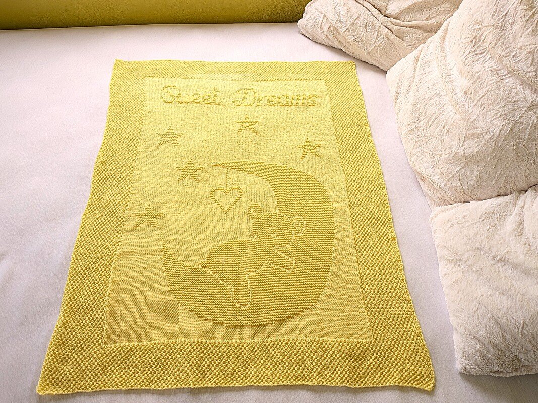 Pale yellow knitted baby blanket with 'Sweet Dreams' text and moon-and-stars motif laid flat