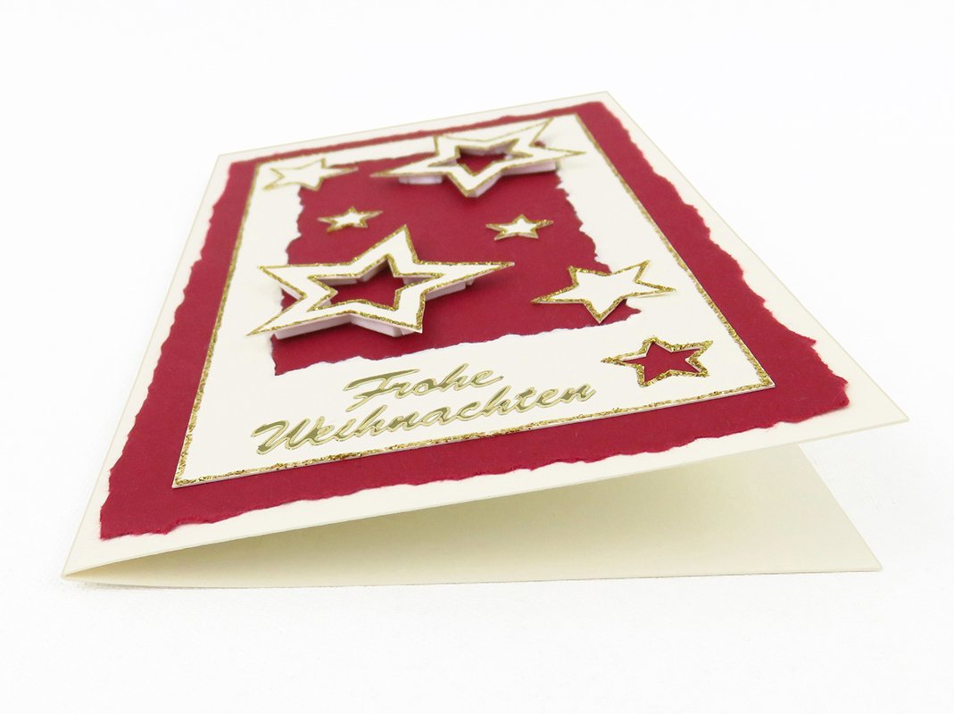Nahaufnahme einer DIY-Weihnachtskarte mit reliefartigen 3D-Sternen, rotem Einleger und goldenen Glitzerrändern