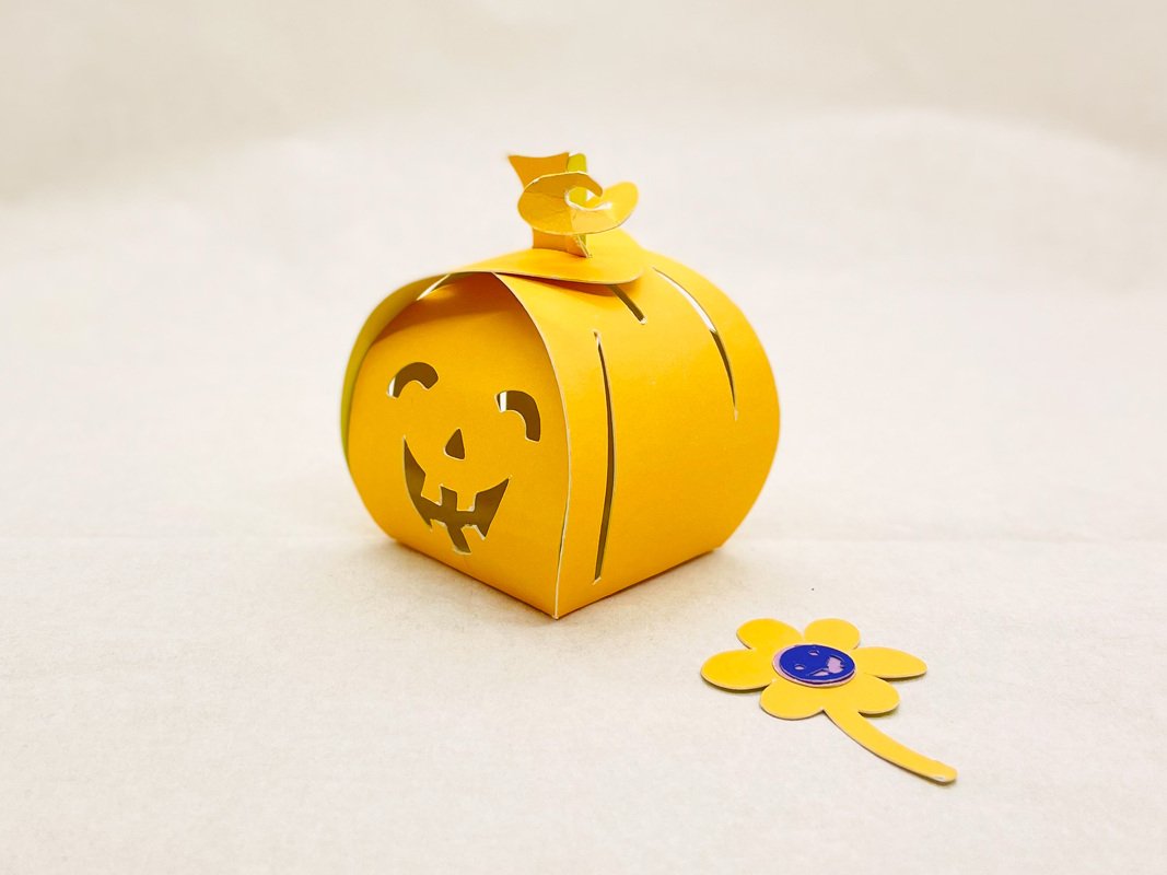 Gelbe kürbisförmige Papierbox mit ausgeschnittenem Gesicht und Papierblume