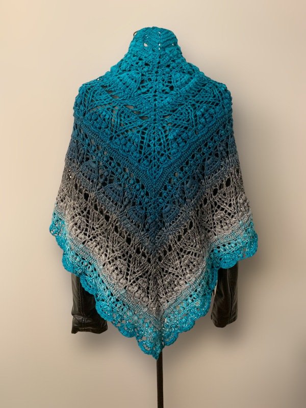 Teal and grey ombre crochet triangle shawl with intricate lace pattern and bobbles displayed on a mannequin.