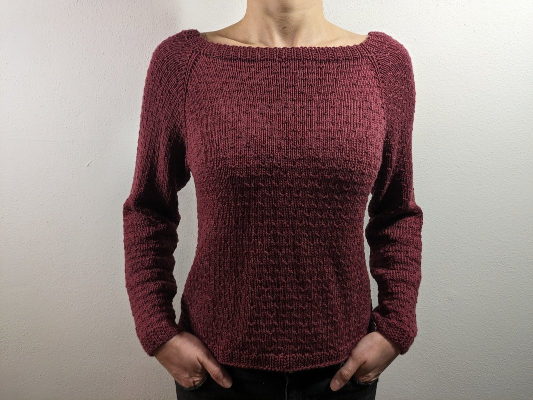 Person trägt dunkelroten, langärmeligen Strickpullover mit U-Boot-Ausschnitt und strukturiertem Muster