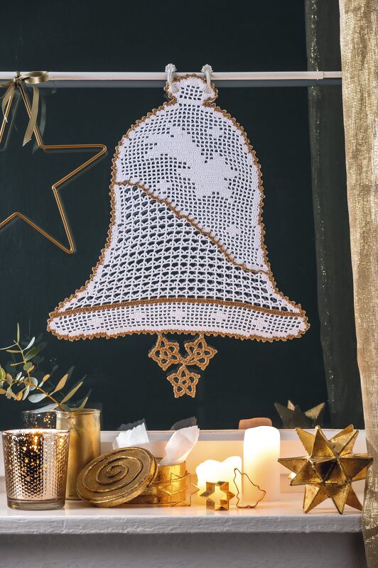 Weiße Häkelglocke mit goldener Umrandung vor dunklem Fenster, dekorativ mit Kerzen arrangiert
