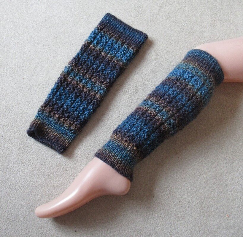 Zwei gestrickte Stulpen in Blau- und Brauntönen, eine am Bein-Mannequin getragen, die andere flach liegend.