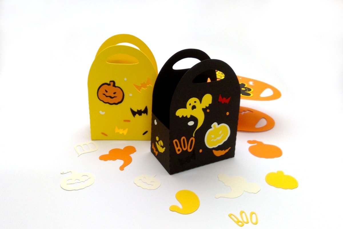 Gelbe und schwarze kleine Papiertüten mit Halloween-Motiven (Kürbis, Geist), umgeben von ausgeschnittenem Papierkonfetti in Orange, Gelb und Weiß