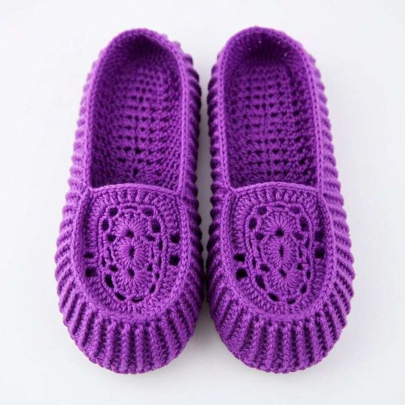 Pair of purple crocheted women's slippers with an openwork decorative toe and ribbed edges on a light background.