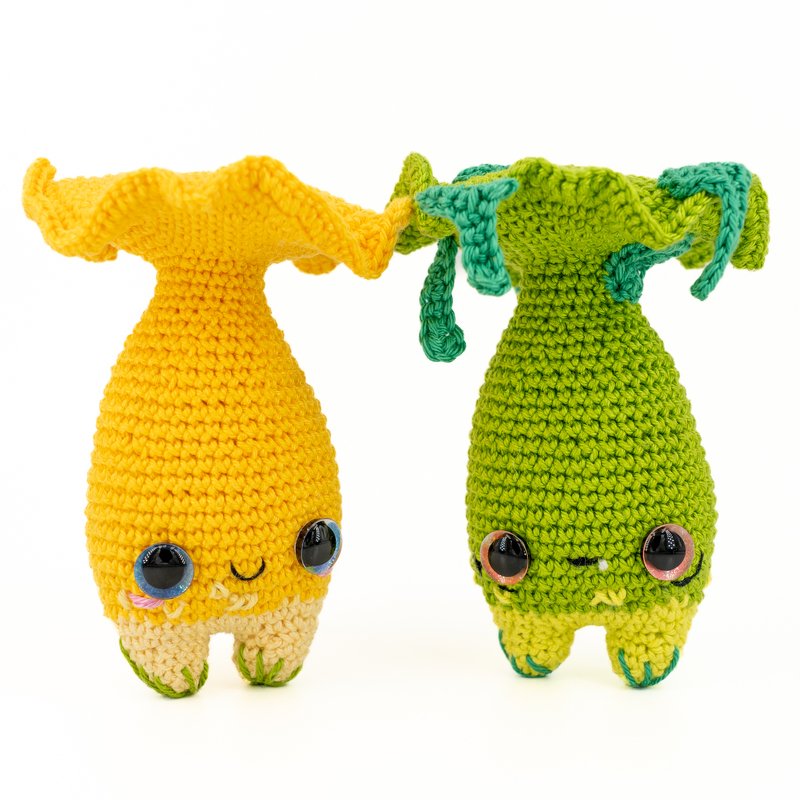 Zwei gehäkelte Amigurumi-Pilzfiguren, eine gelb und eine grün, auf weißem Hintergrund