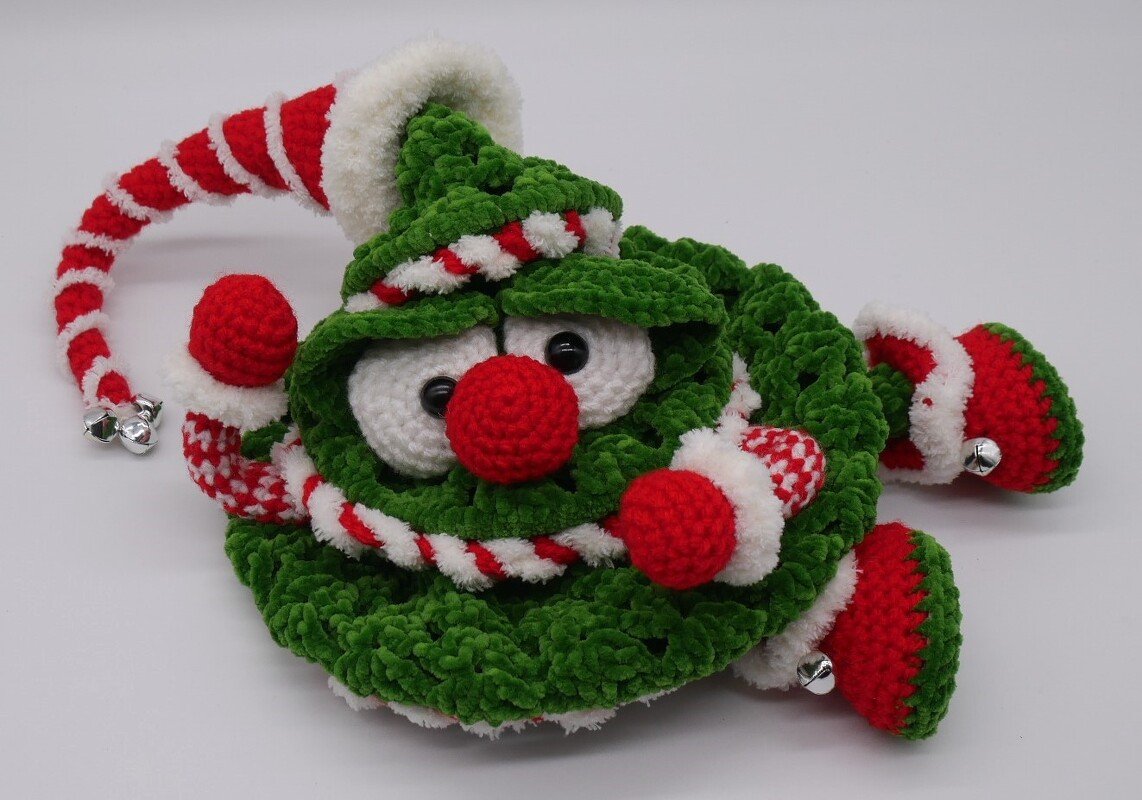 Gehäkelter grüner Weihnachtswichtel mit roter Nase, geringelter Mütze und Glöckchen vor weißem Hintergrund.
