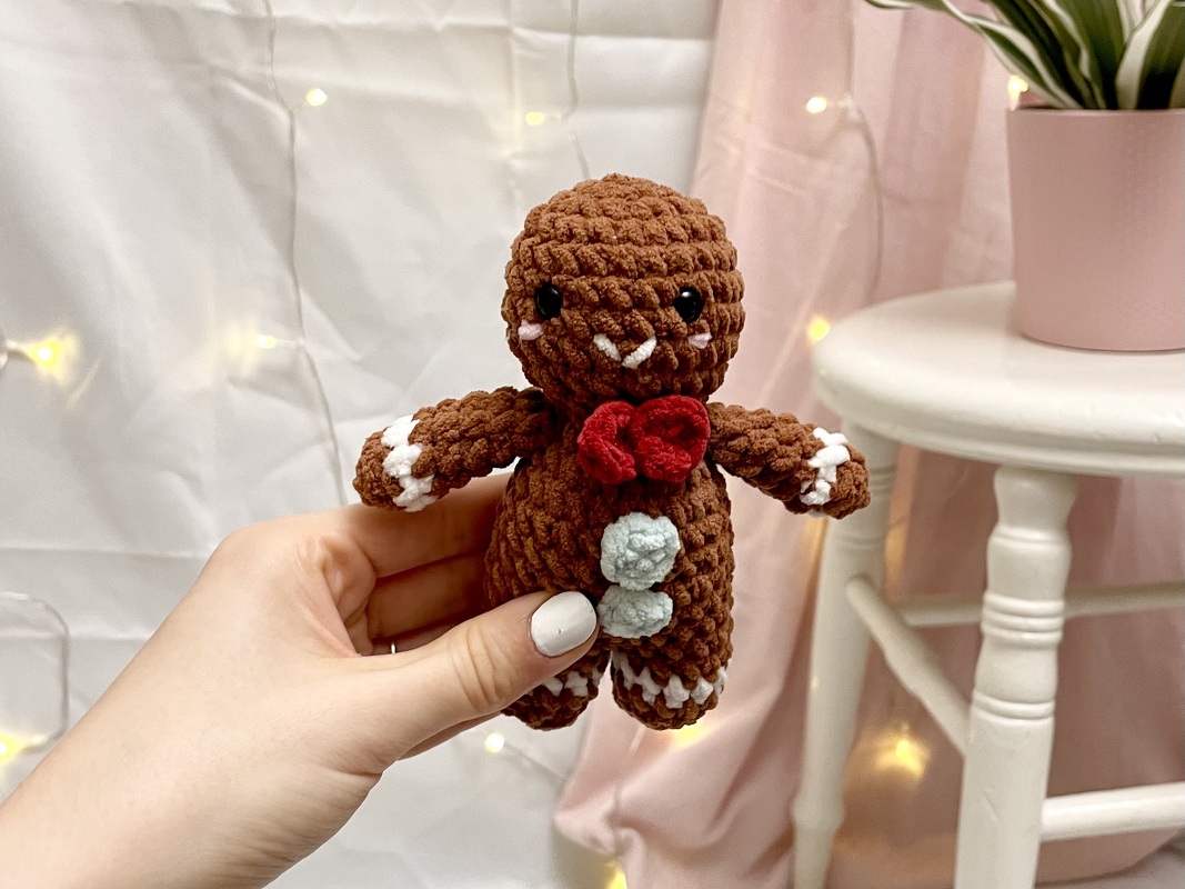 Gehäkelter Lebkuchenmann mit roter Schleife und hellblauen Knöpfen, von Hand gehalten