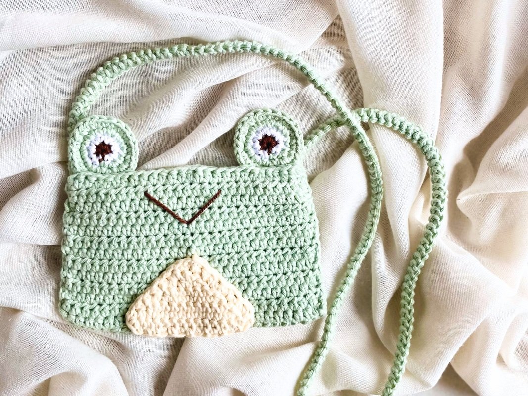 Hellgrüne gehäkelte Umhängetasche in Froschform mit applizierten Augen und hellem Bauch