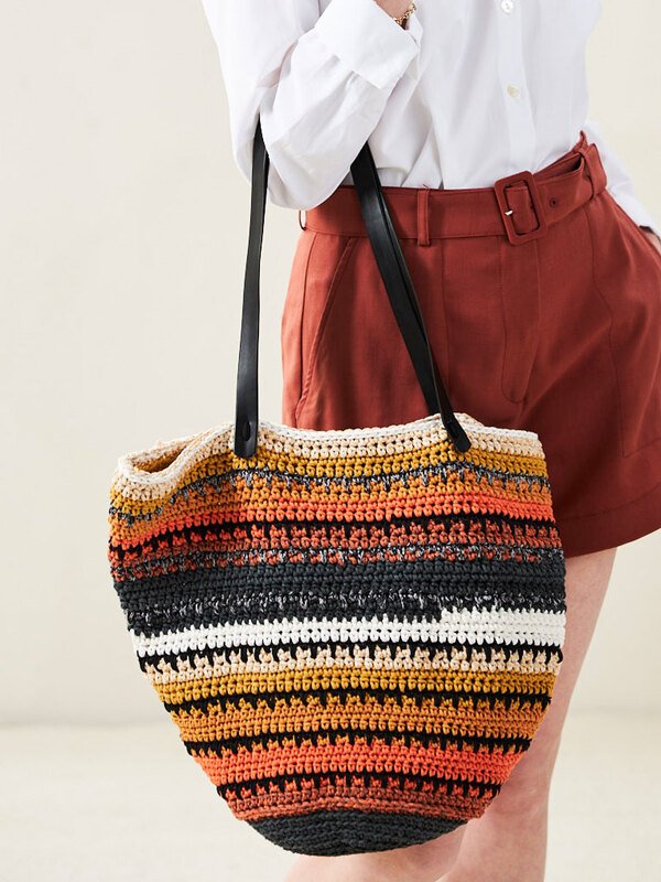 Gehäkelte Shopper-Tasche mit horizontalen Streifen in Orange, Gelb, Schwarz und Weiß, an der Schulter getragen.