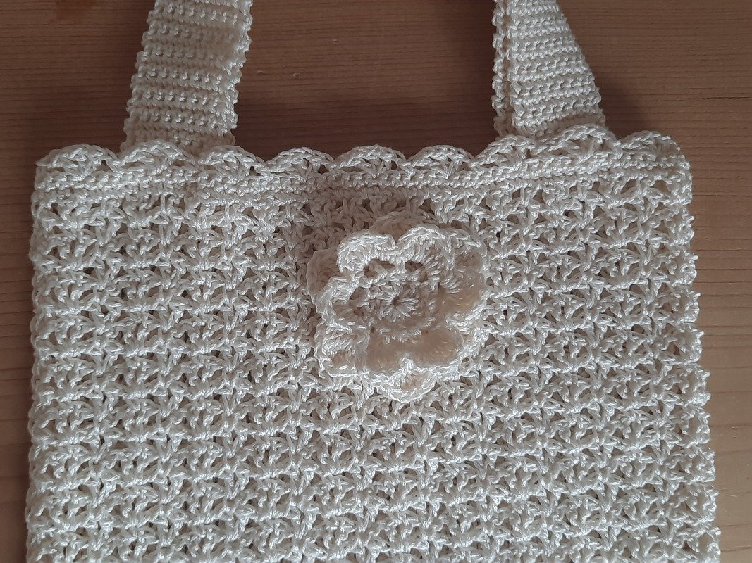 Cremefarbene, gehäkelte Henkeltasche mit Lochmuster und gehäkelter Blüte