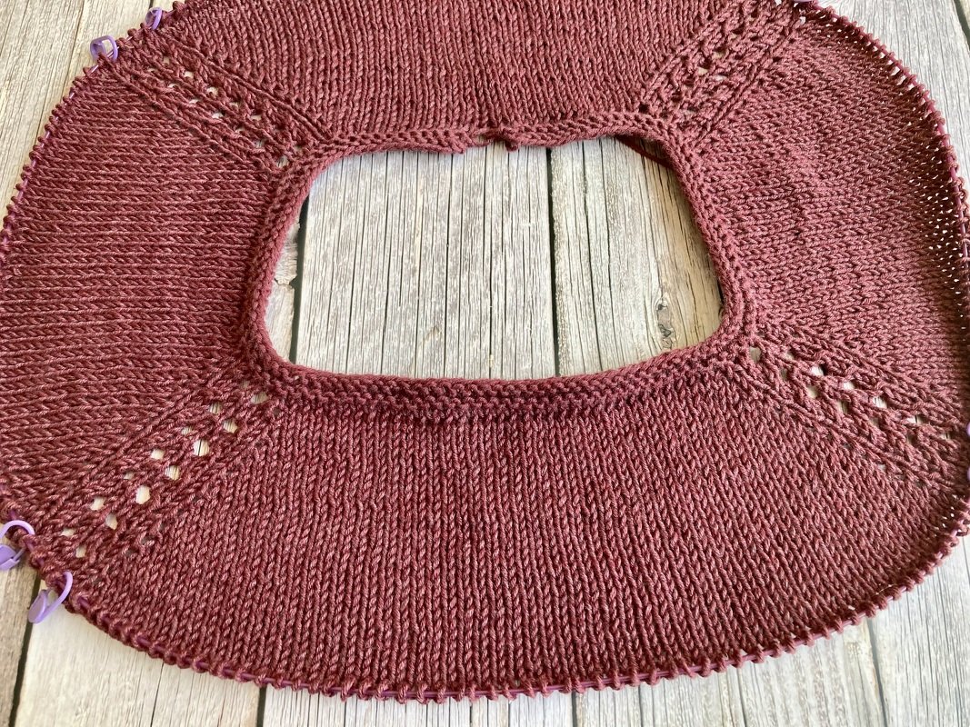 Nahaufnahme einer kastanienroten, von oben gestrickten Rundpasse mit Raglanzunahmen und Maschenmarkierern