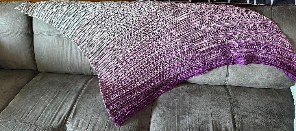 Handgehäkeltes Dreieckstuch mit diagonalem Lochmuster, Farbverlauf Hellgrau zu Lila auf Sofa